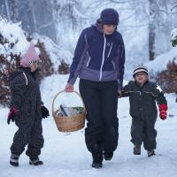 Mor med sine to børn, der går en tur i skoven, som er dækket af sne