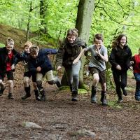 På billedet ses en flok glade skoleelever, der løber i skoven og leger