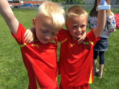 To drenge i rødt fodboldtøj holder hinanden om armen og smiler