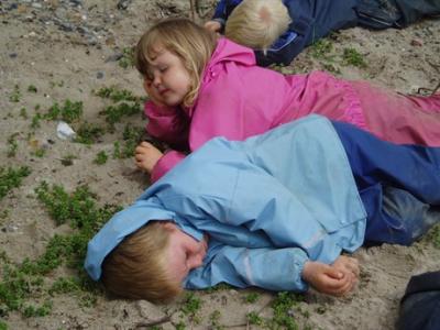 3 børn ligger og slapper af på jorden. Den ene dreng sover
