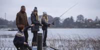 En familie med to teenagepiger står på en bro og fisker med fiskestænger
