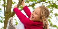 På billedet ses en pige, der klater i træer. Hun smiler