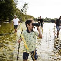 foto af dreng med kikkert i sø og flere mennesker bagved